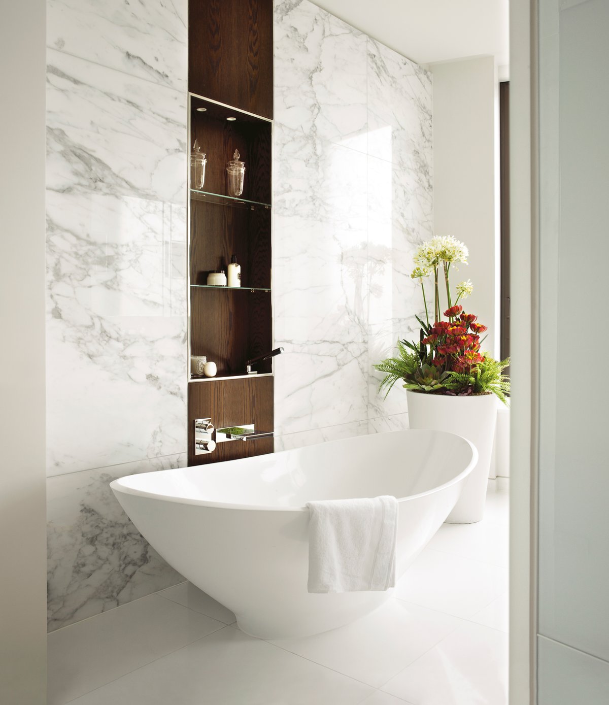 Compact luxury bathroom scheme — Calacatta marble feature wall, dark walnut storage niche, BC Designs Aurelius freestanding bath, chrome wall-mounted basin mixer