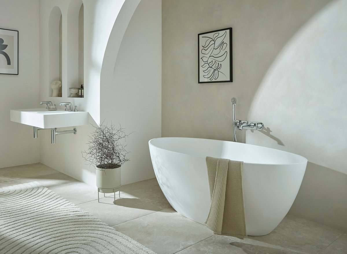 Double-ended freestanding bath placed across joist run with generous clear floor space, basin alcove twin mirrors lit by vertical wall-lights at face height