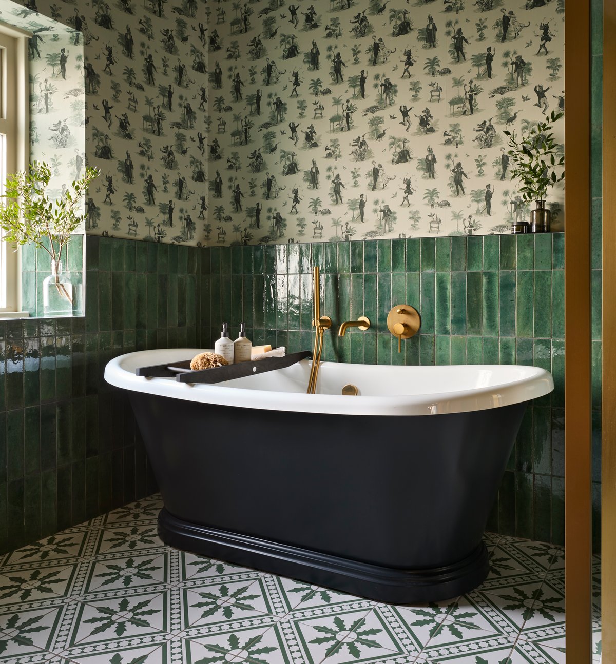 Period-property luxury scheme — BC Designs painted black slipper boat bath, emerald green metro tile dado, toile-de-Jouy wallpaper above, heritage encaustic tile floor, brushed brass wall-mount bath filler — non-standard period detailing requiring designer coordination