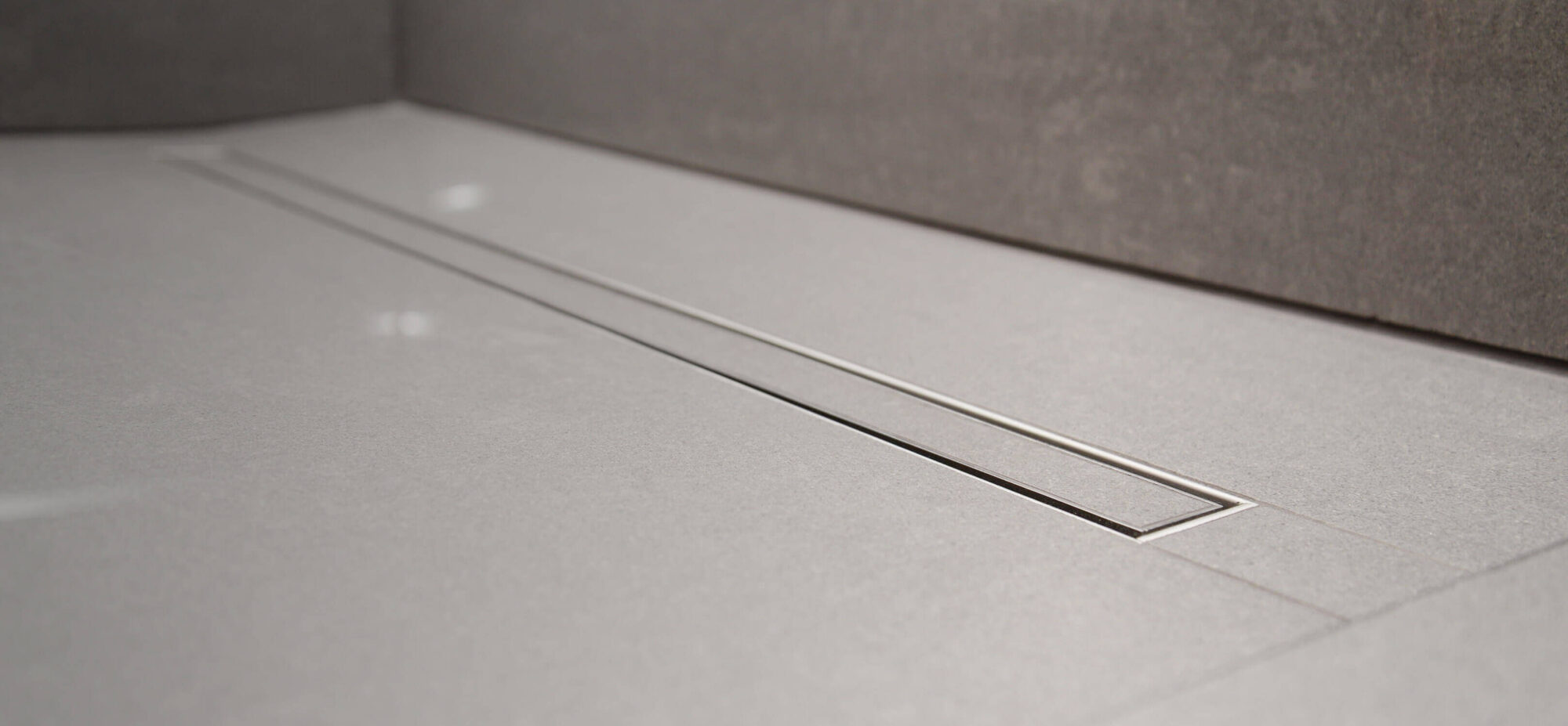 UK wet room build-up - On The Level pre-formed wet-room substrate former with built-in gradient fall to a linear drain, full-floor tanking and large-format porcelain tile carrying continuously across the floor without a tray or kerb