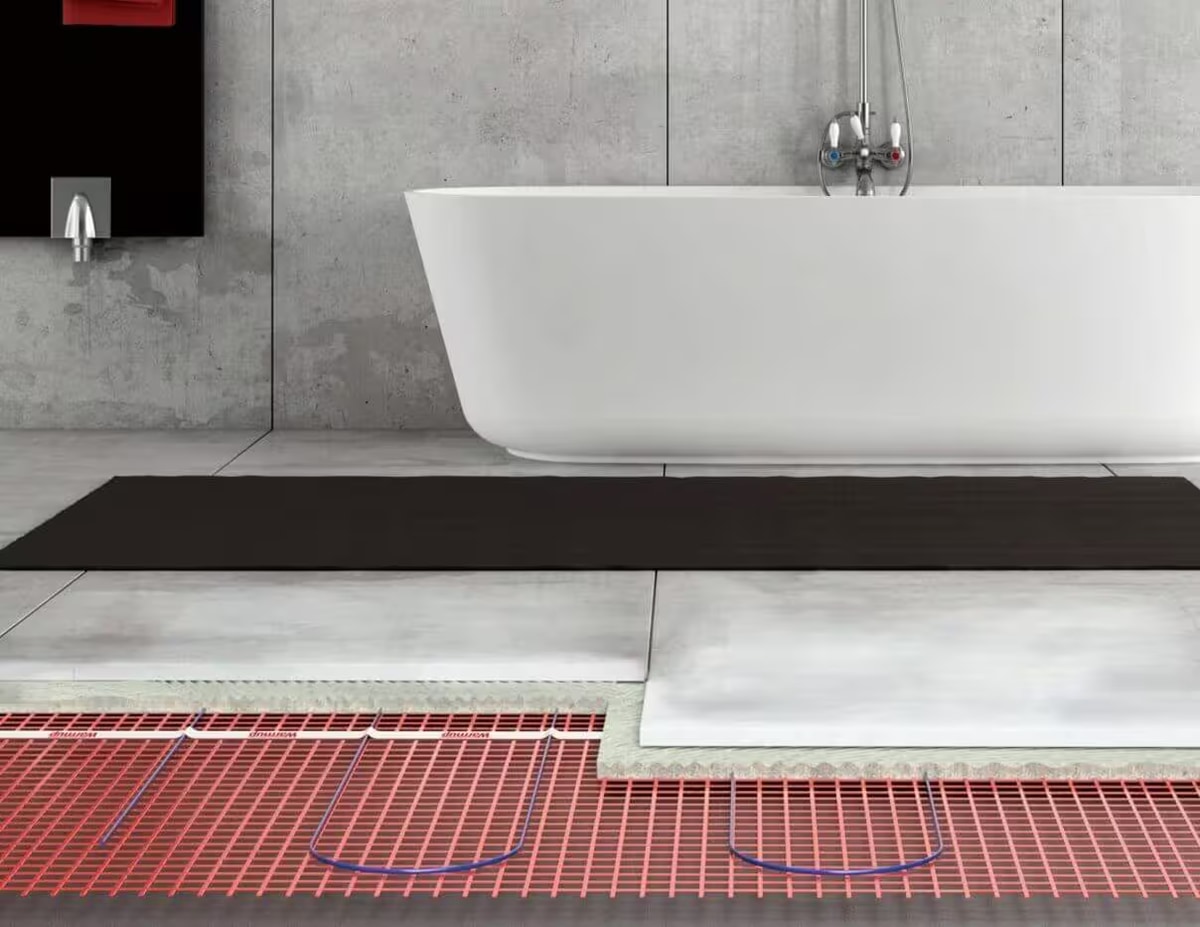 Warmup electric underfloor heating mat being unrolled across a bathroom floor before tile adhesive - pre-spaced heating element on a self-adhesive carrier mat for a single-afternoon install in UK retrofit bathrooms