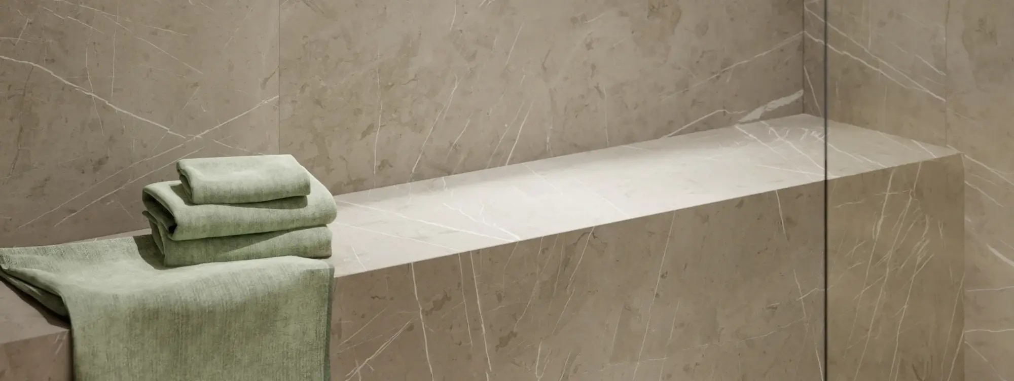Steam shower vs sauna vs wet room: stone-effect bench built into a tanked shower wall, sage-green towels folded over one end