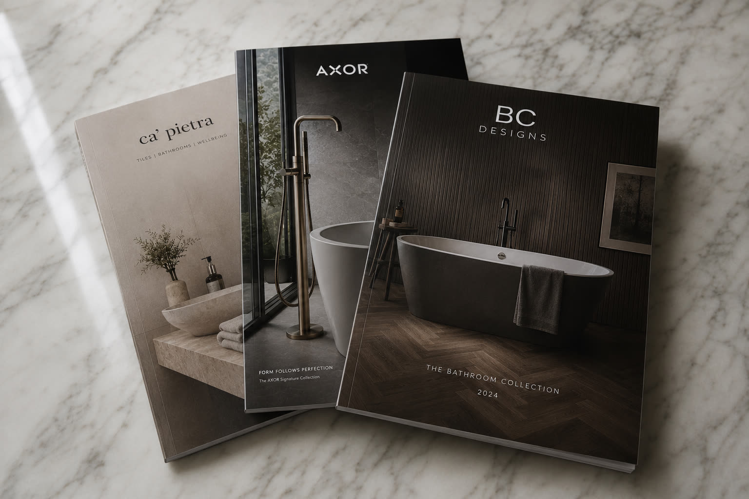 Bowman Bathrooms brochure collection — Ca' Pietra, AXOR and BC Designs catalogues laid out on a marble surface