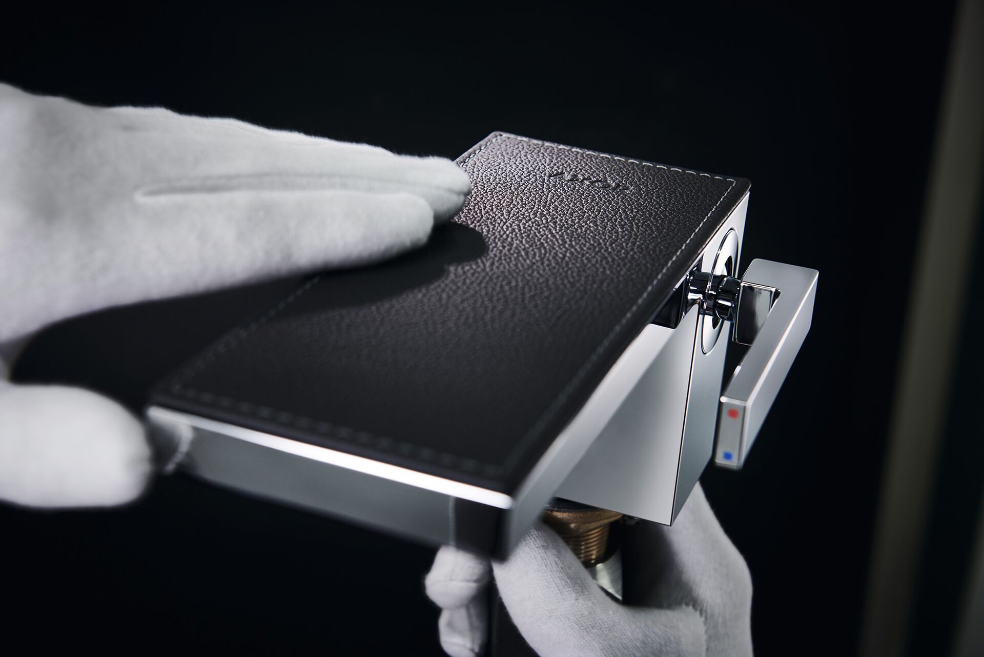 Gloved hands fitting a black leather cover plate to an AXOR MyEdition mixer.