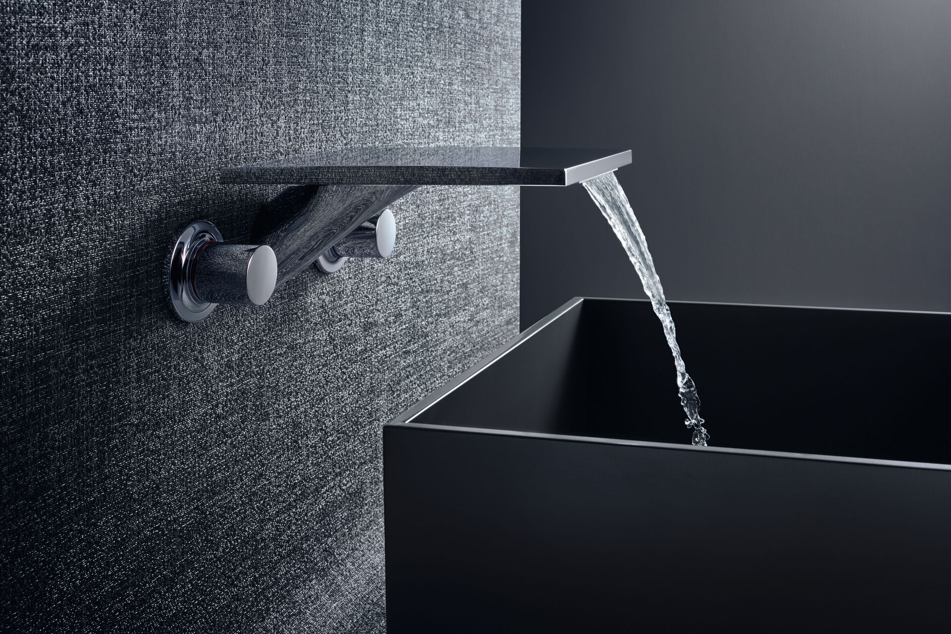 Wall-mounted AXOR Massaud mixer sending water into a dark rectangular basin