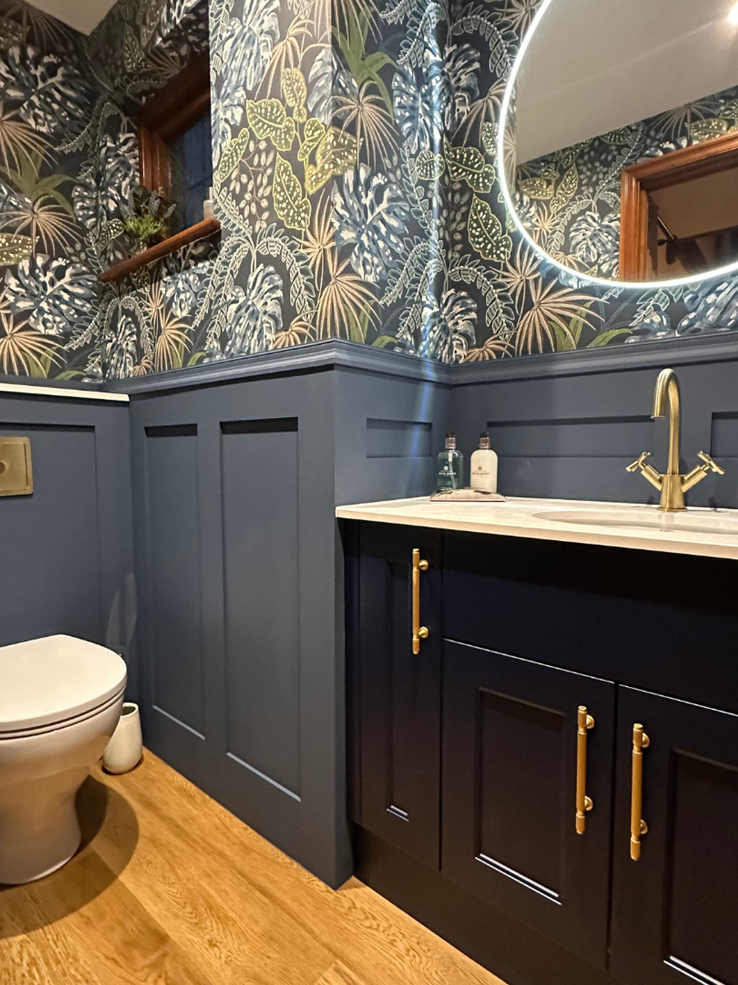 Renovated downstairs toilet with navy panelling, jungle wallpaper and brass flush plate, same footprint