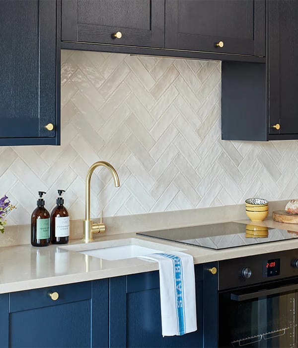 White herringbone tile splashback behind a kitchen worktop with warm wood shelving