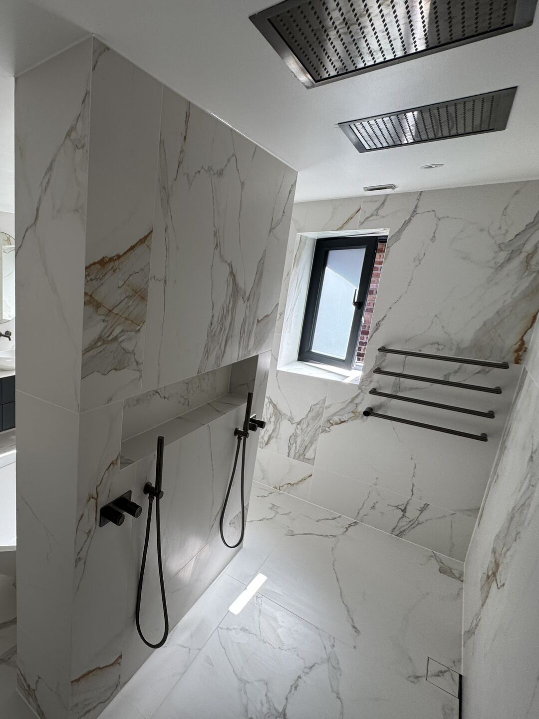 Two recessed rectangular rain heads in the ceiling above an open shower, with two brushed black handsets on hoses either side of a long tiled niche, Billericay CM11 master ensuite