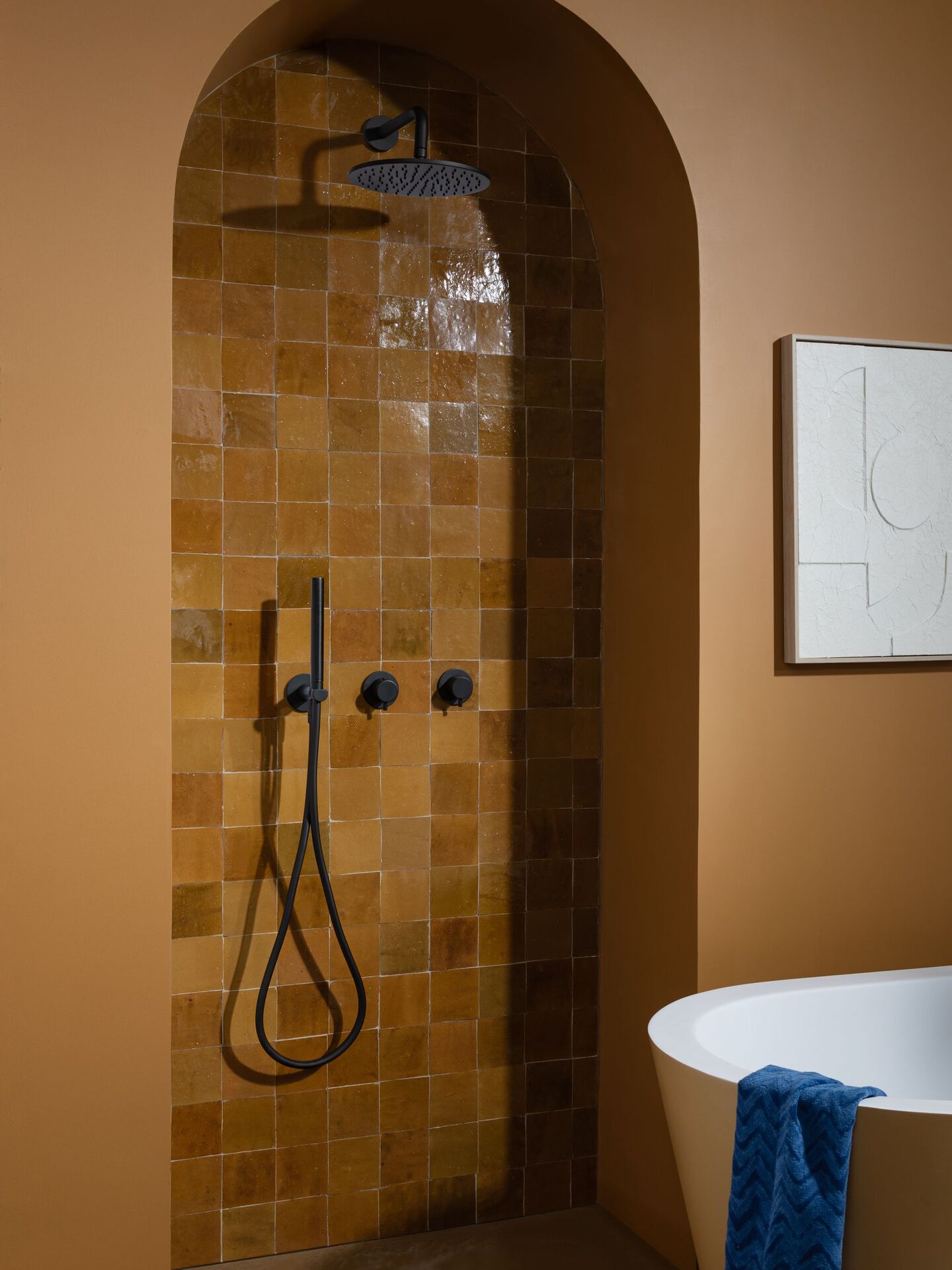 Matt black wall-mounted rain shower head and handset on concealed controls in a tiled arched recess, JTP VOS range