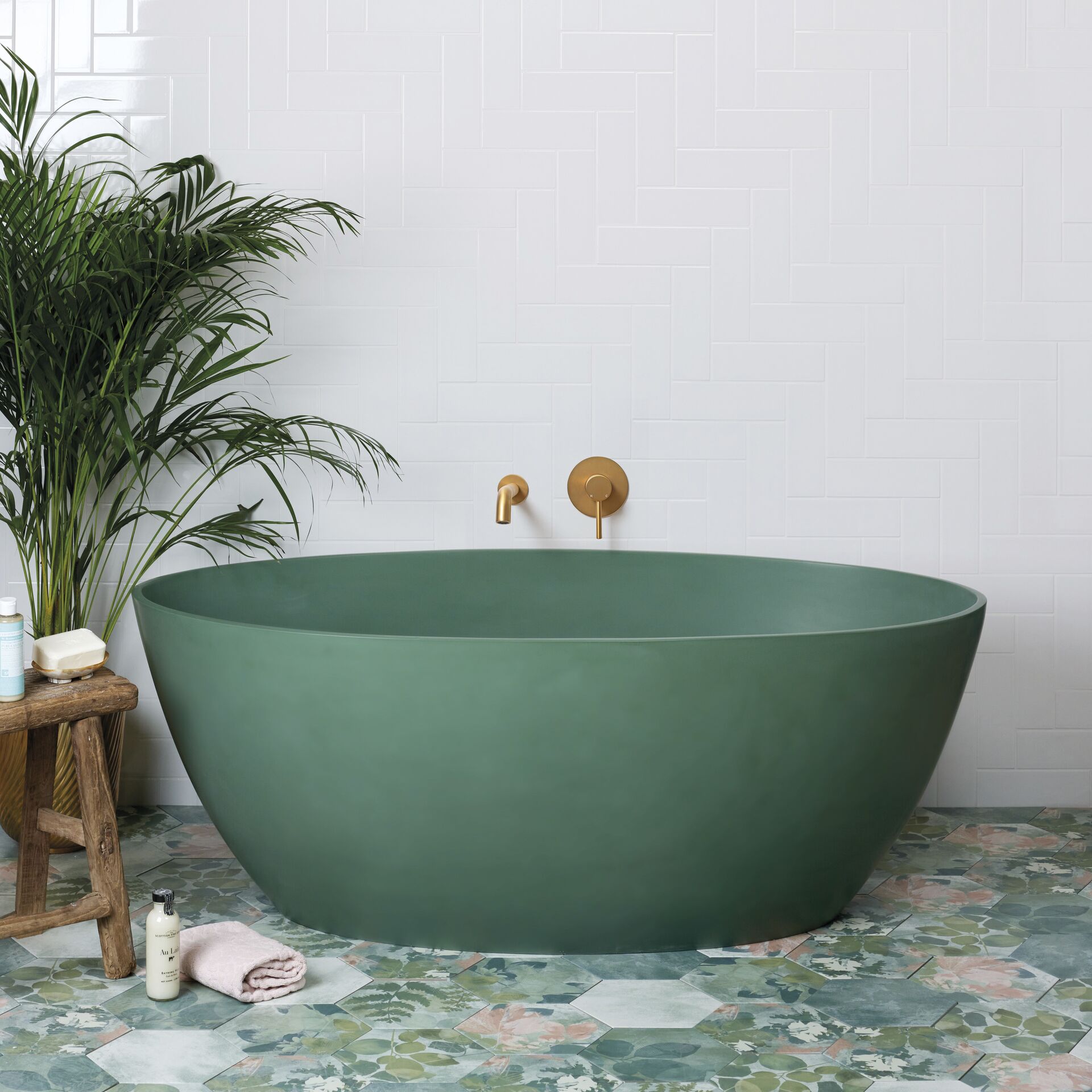 Green freestanding bath with brass wall controls and floral floor tiles