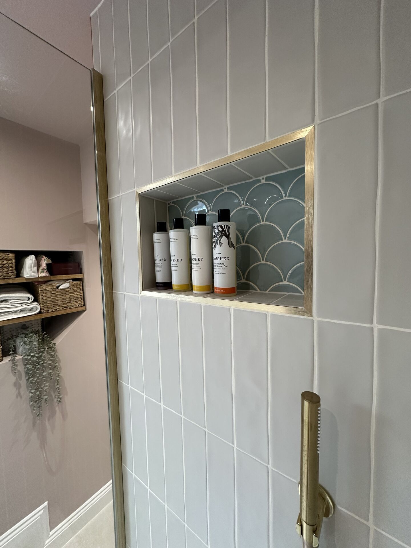 Four toiletry bottles standing upright in a fishscale-tiled shower niche with a brushed brass trim, Great Waltham CM3 family bathroom