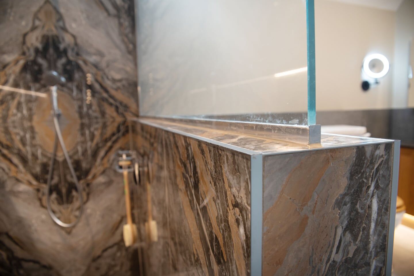 Glass shower screen set into a trimmed half-height tiled wall with bookmatched stone behind, Halstead CO9 master ensuite