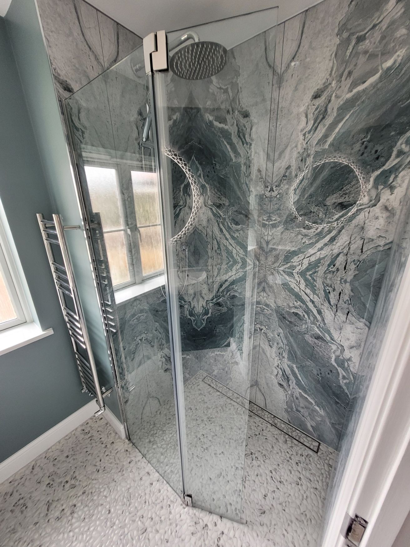 Pebble-effect Porcelanosa Boulder floor tile with a slim linear drain flush to the surface, beneath a bookmatched stone-look shower wall, Highwoods CO4 wetroom ensuite