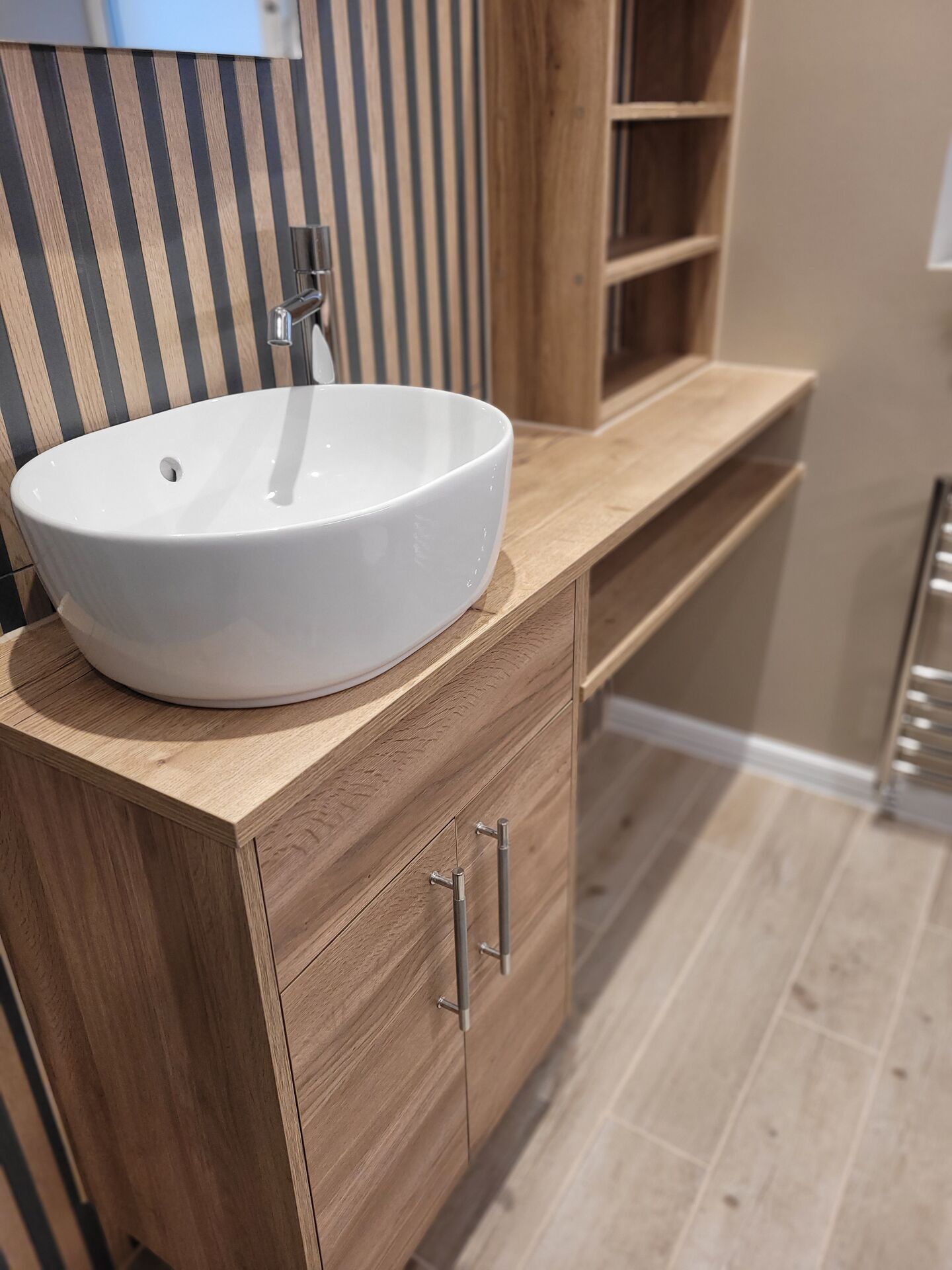Roper Rhodes oak-effect fitted furniture with an oval vessel basin and tall chrome mixer in a Benfleet SS7 ensuite — the product quality we supply to Rayleigh homes