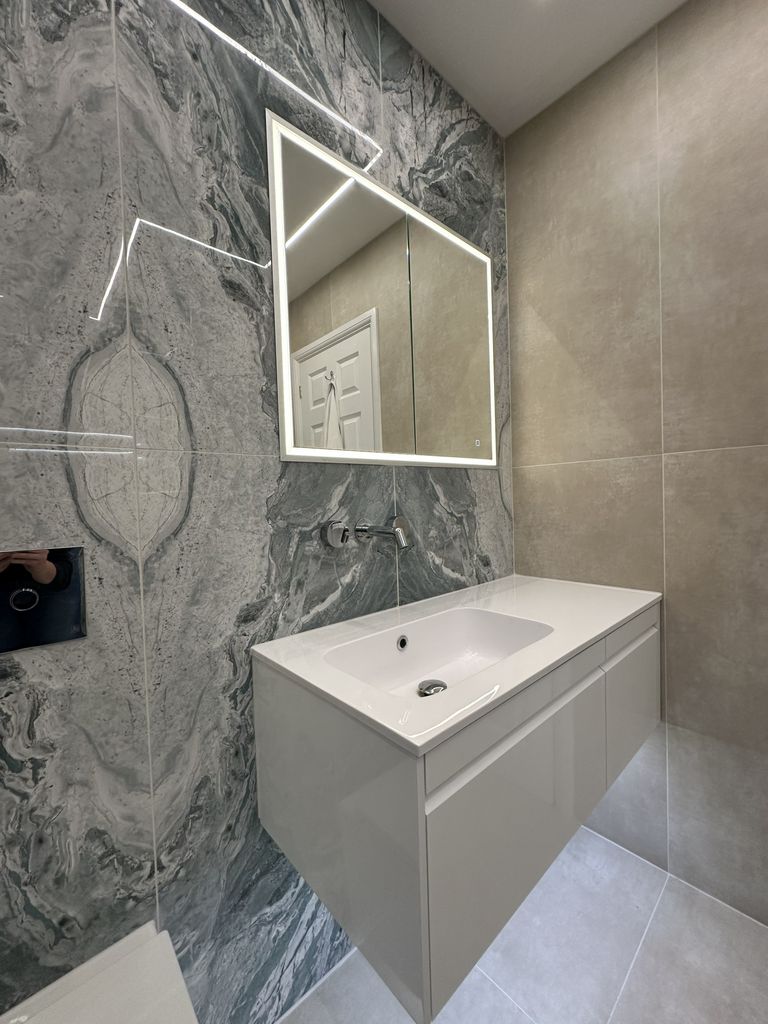 Illuminated mirror cabinet and wall-hung basin against bookmatched stone in a Braintree CM7 luxury ensuite wetroom