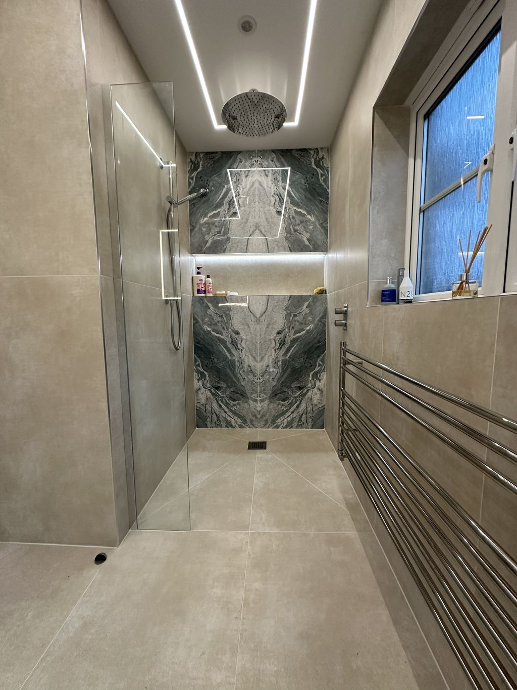 Wetroom shower zone with JTP ceiling rainfall head, LED-lit niche, Lakes frameless glass screen, and JIS Europe towel radiator in Braintree CM7