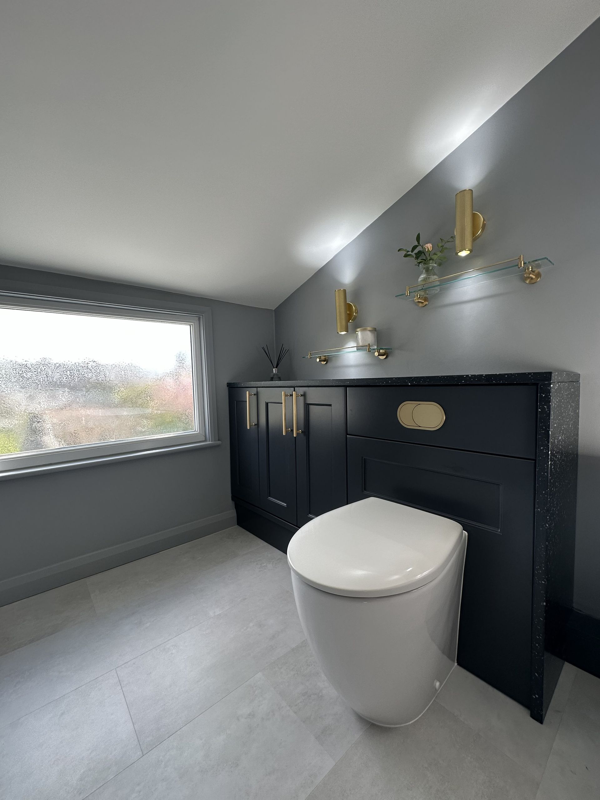 Rimless back-to-wall WC in dark navy fitted furniture with brushed brass flush plate and speckled quartz worktop in Braintree CM7 bathroom