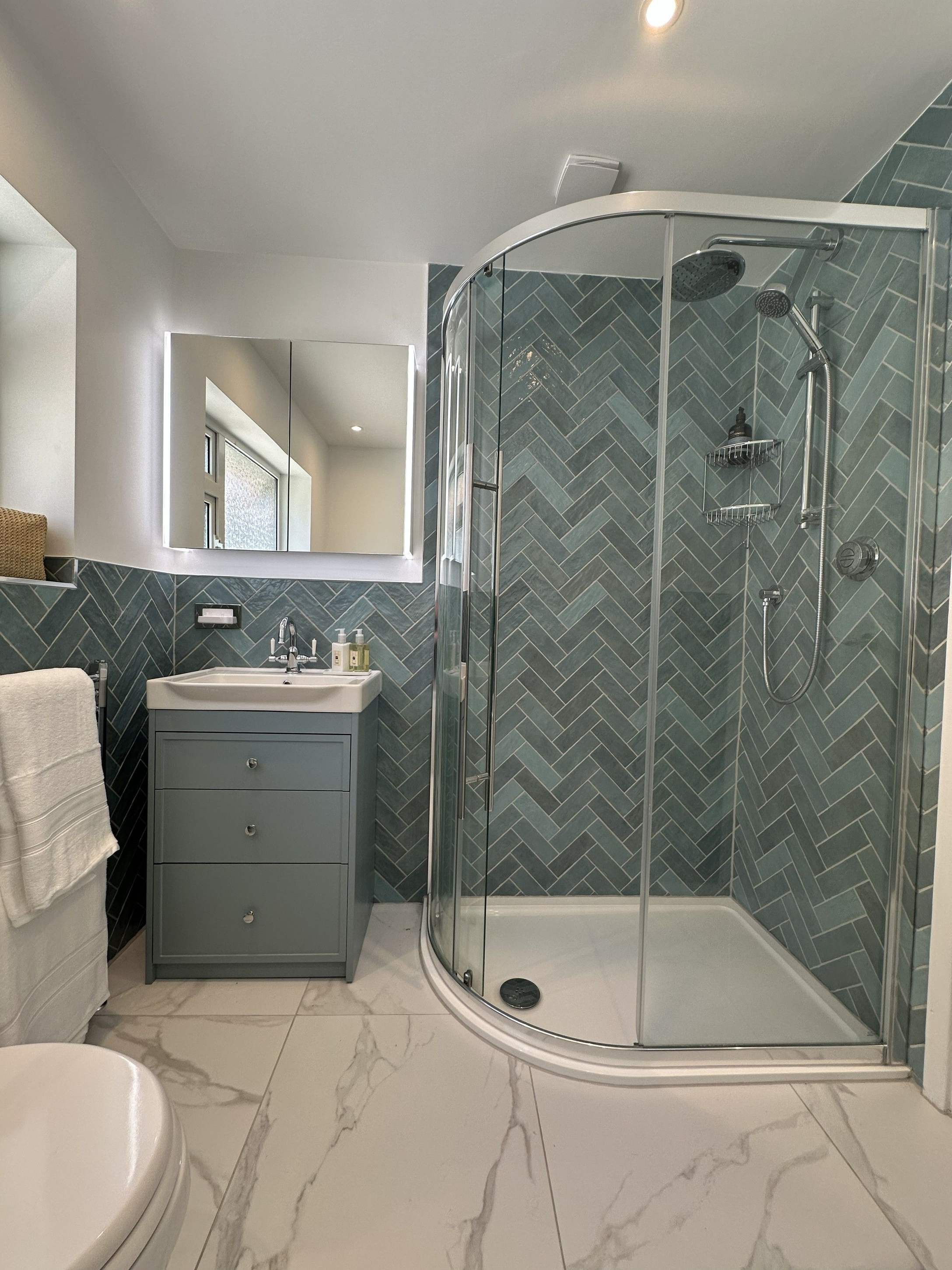 Herringbone wall tiles with towel rail detail in Brentwood CM13 bathroom designed by Bowmans