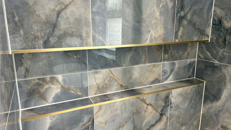 Brushed-brass trimmed recessed niches cut into blue onyx Ca' Pietra tiles in a Brentwood CM13 wetroom shower