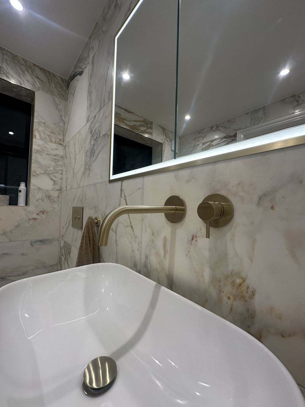 JTP brushed brass wall-mounted tap above vessel basin with honed marble wall and HiB Vanquish mirror Chelmsford CM3