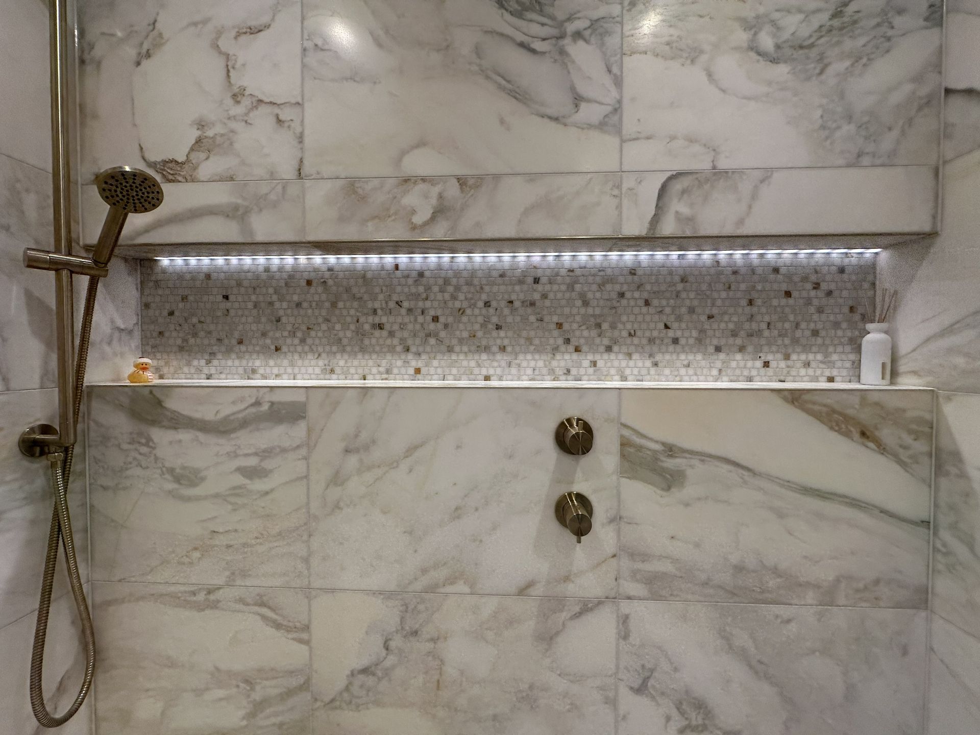 LED-lit mosaic shelf with JTP brushed brass hand shower and valve controls inside wetroom Chelmsford CM3