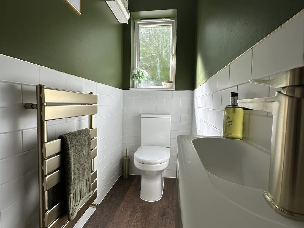 Full room view showing Hix brass radiator, Charlotte WC, dark wood-effect floor and white metro tiles Great Leighs CM3