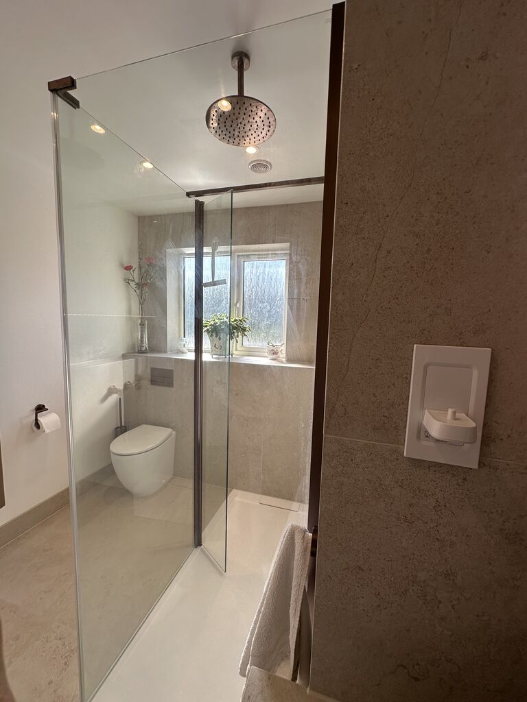 Brushed bronze rain shower head above walk-in enclosure with wall-hung WC beyond Great Notley CM77 Essex