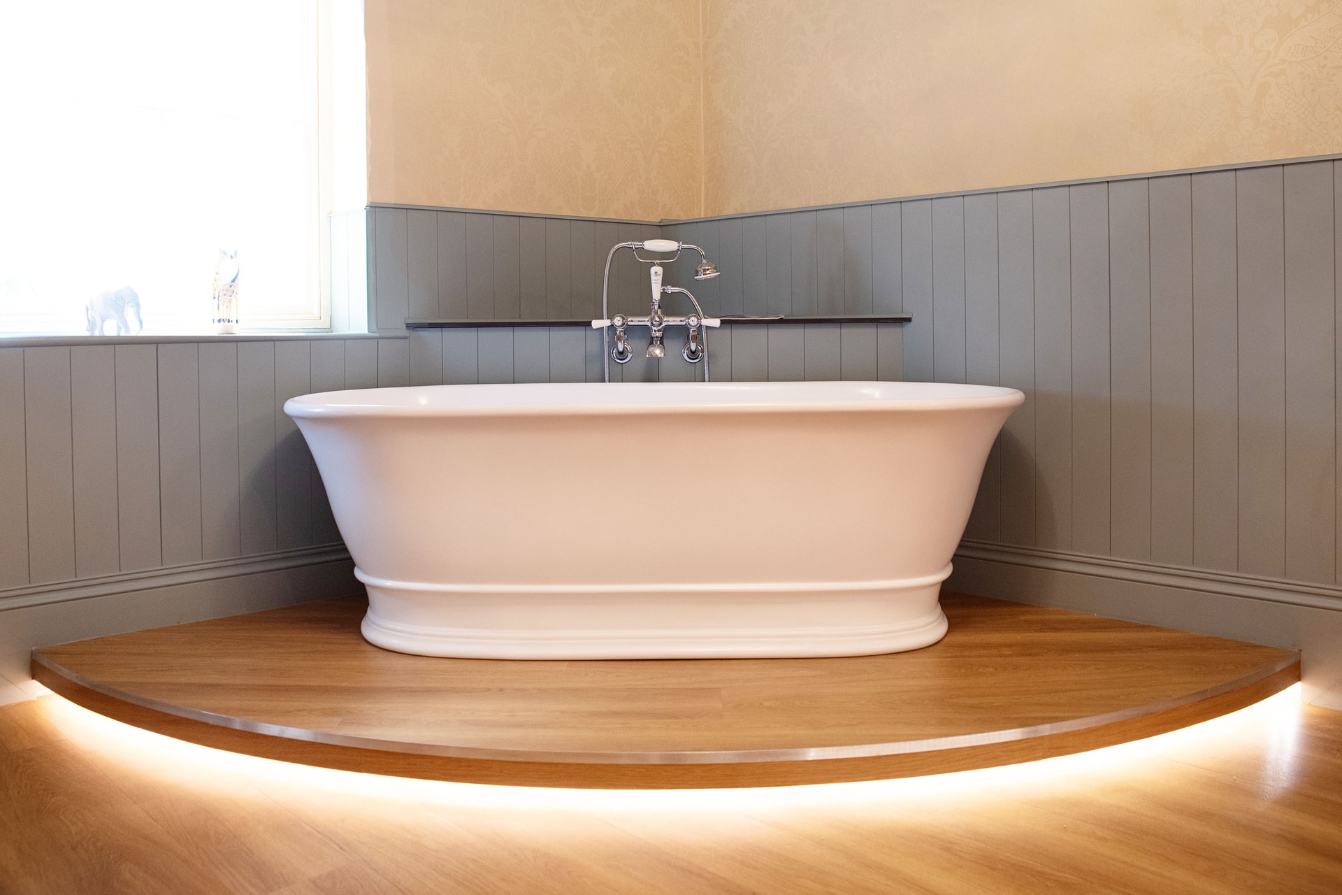 BC Designs Brampton freestanding bath on curved oak ledge with LED strip lighting, blue panelling and yellow wallpaper Halstead CO9
