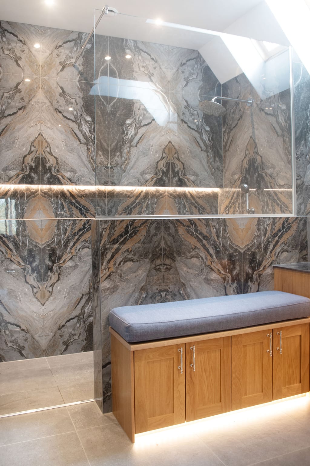 Custom Calypso oak bench with grey cushion below frameless glass and bookmatched Nero feature wall Halstead CO9