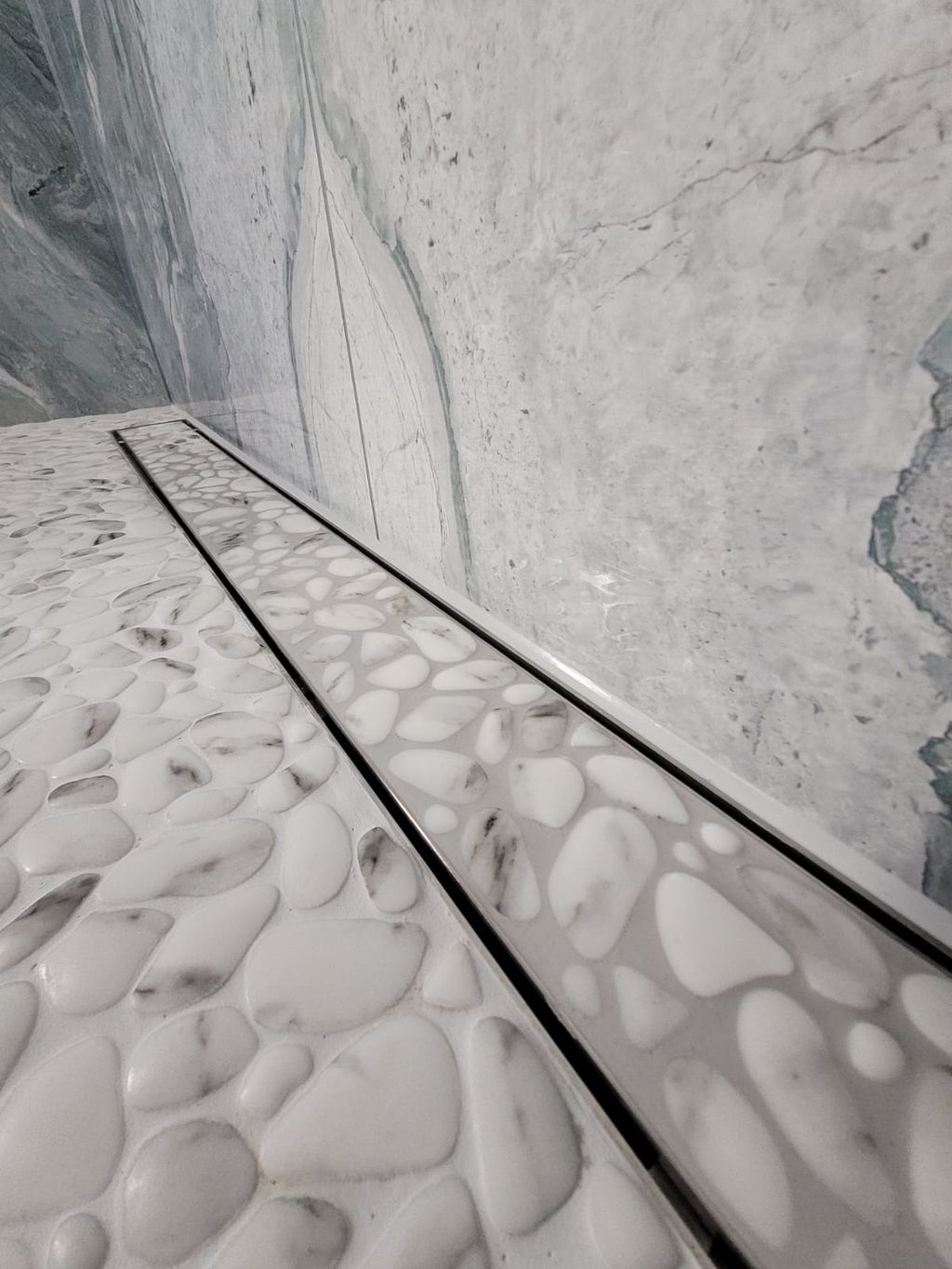 Linear drain close-up with Porcelanosa Boulder pebble floor tiles and Ocean Magnifique wall Highwoods CO4
