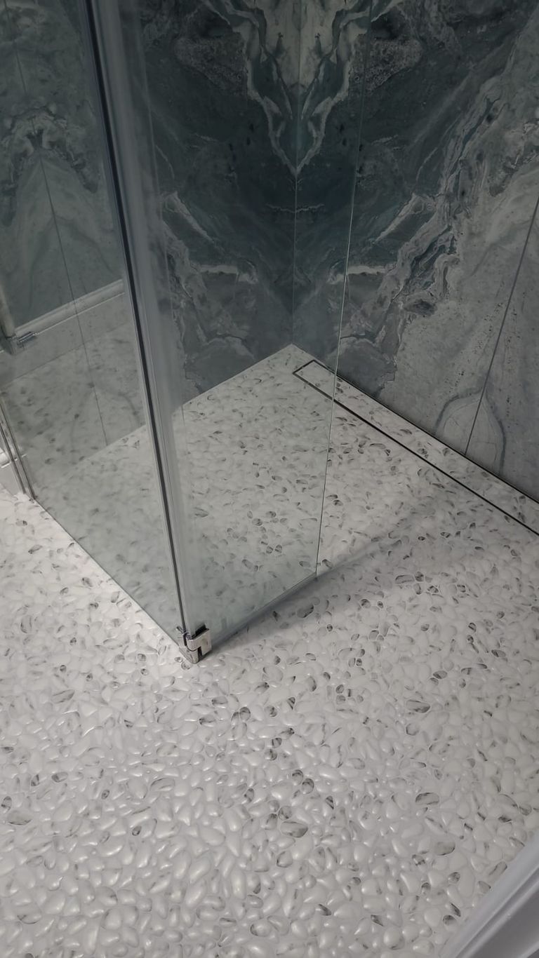Frameless glass shower screen meeting the pebble wetroom floor beneath bookmatched slabs in the Highwoods CO4 ensuite