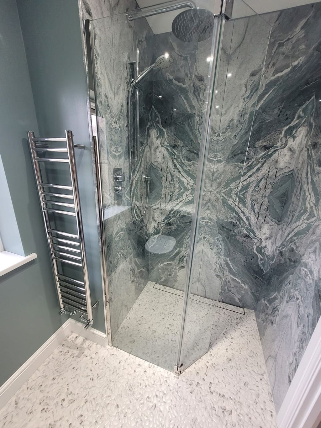Wetroom shower zone with Ocean Magnifique bookmatched slabs, chrome towel rail, and glass screen Highwoods CO4
