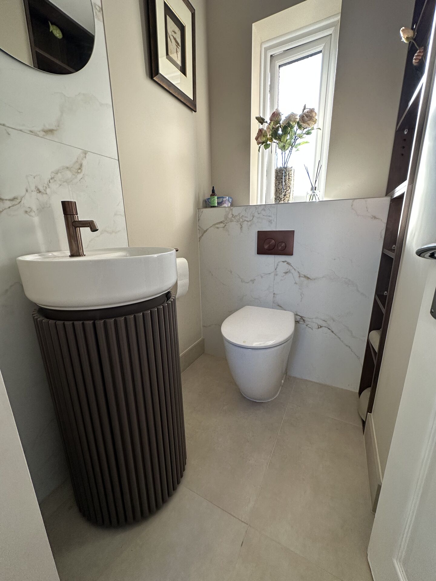 Fluted walnut basin unit, bronze-coloured tap and pale marble-effect tiles in a Kelvedon cloakroom