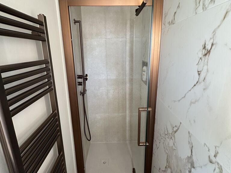 Kelvedon CO5 master ensuite with bronze-framed shower and marble-look porcelain