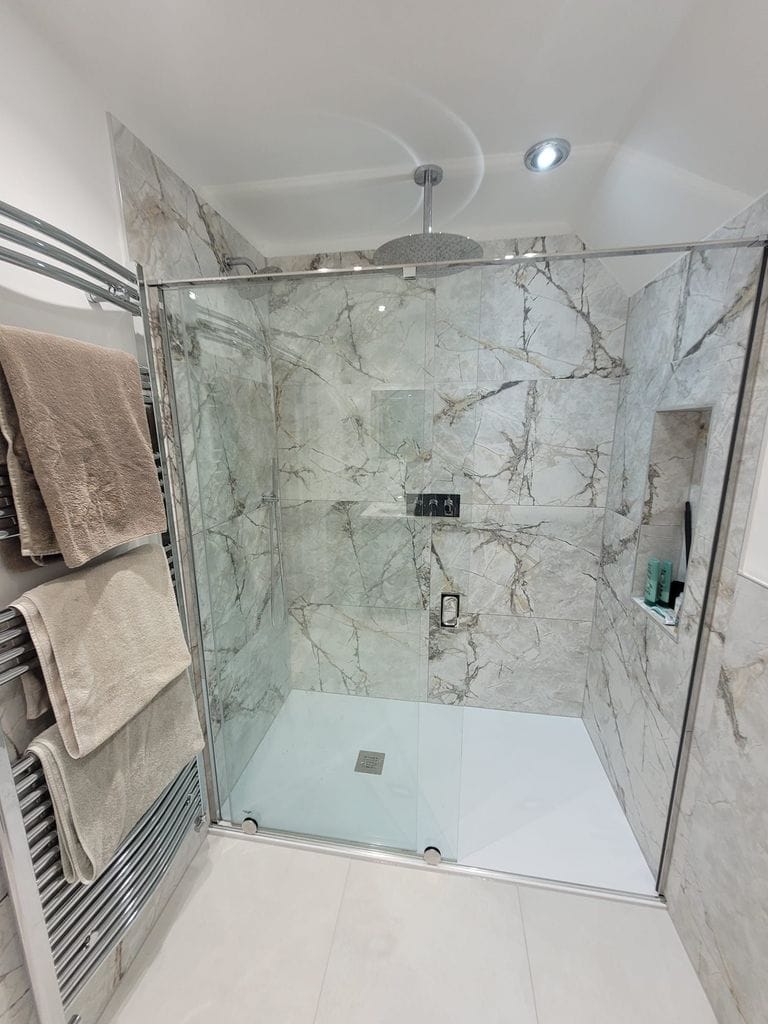 Walk-in shower enclosure with ceiling rain head Ca' Pietra marble tiles and recessed niche Tiptree CO5