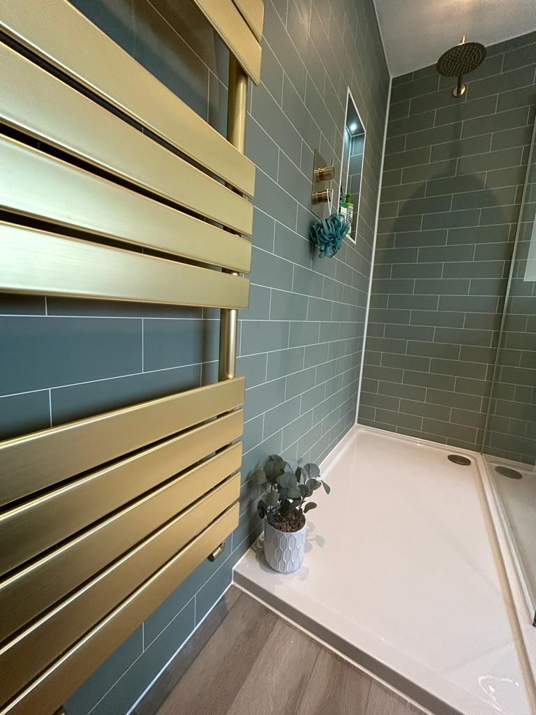 JTP brushed brass heated towel radiator beside Fibo-panelled shower with rain head West Mersea CO5