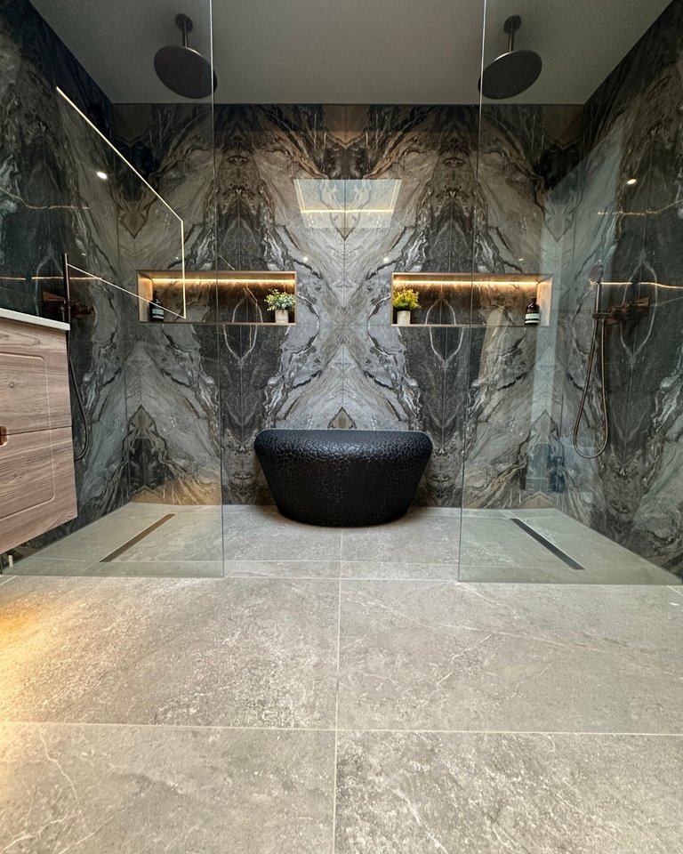 Dual his and hers ceiling rain showers with bookmatched marble tiles LED niches and Porcelanosa pebble bench West Mersea CO5