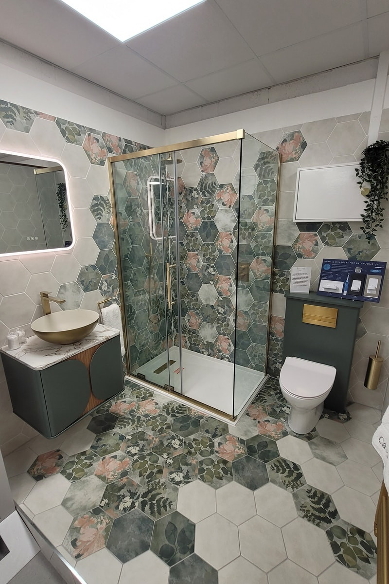 Floral hexagon tiled shower pod with brass enclosure, gold vessel basin and green vanity inside the Bowmans Braintree showroom